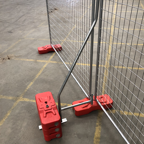 Temporary fencing panel secured in place by red weighted fence feet and metal bracing support, set up on a concrete surface in an indoor area.